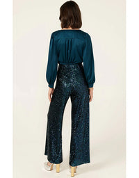 Woman wearing a teal blouse and sequin pants on a white background