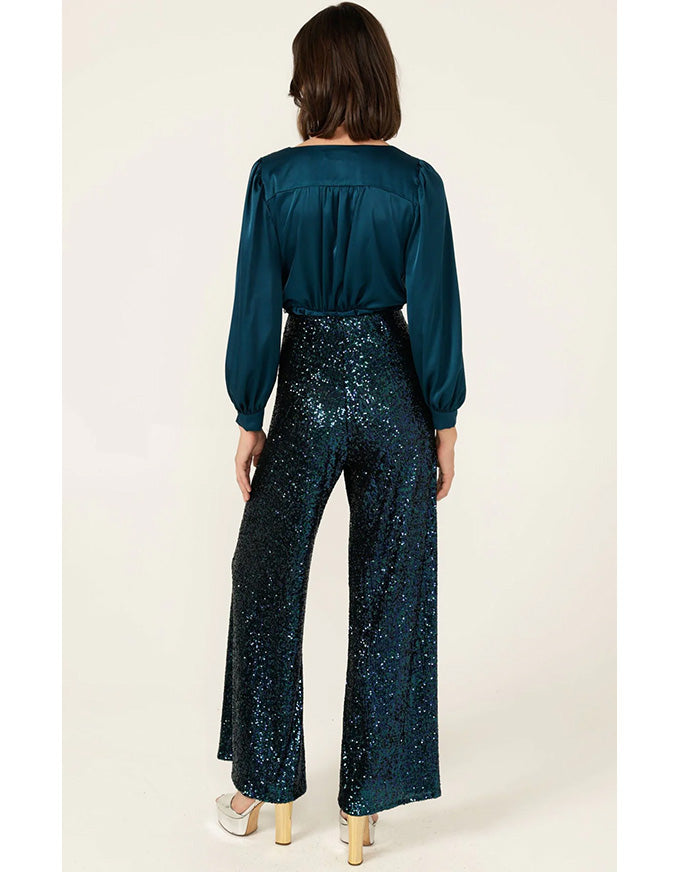 Woman wearing a teal blouse and sequin pants on a white background