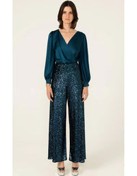 Woman wearing a teal blouse and dark blue patterned pants on a white background