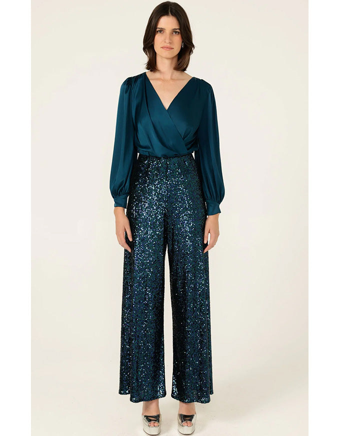 Woman wearing a teal blouse and dark blue patterned pants on a white background