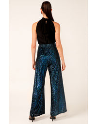 Woman wearing a black sleeveless top and blue sequin pants on a white background