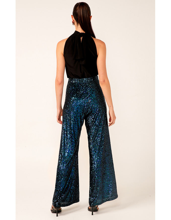Woman wearing a black sleeveless top and blue sequin pants on a white background