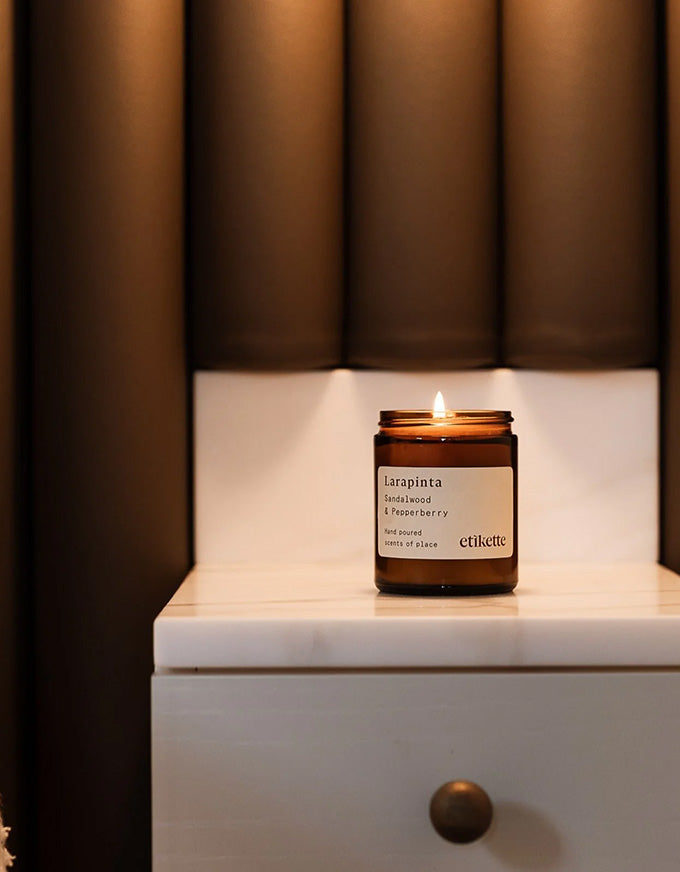 Candle in a glass jar on a white surface with a brown curtain in the background