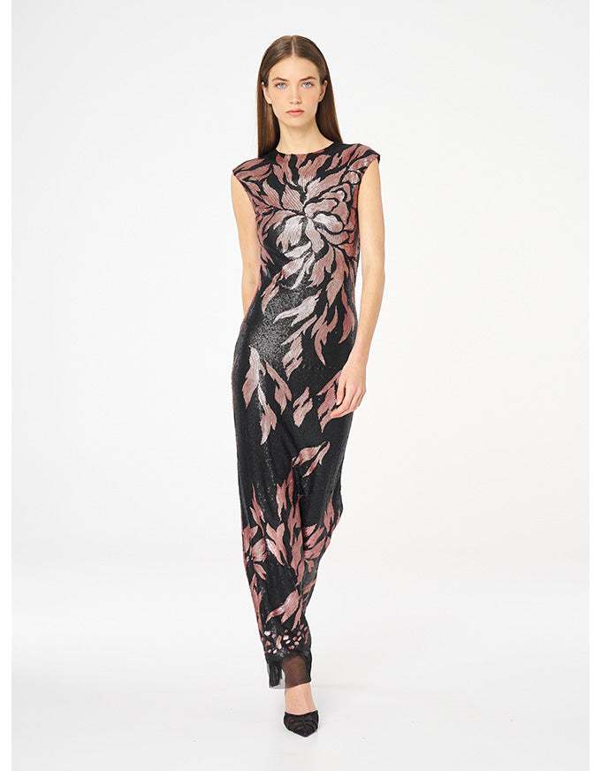 A model wearing a sleeveless black maxi dress with a pink and gray floral pattern, standing against a plain white studio background.