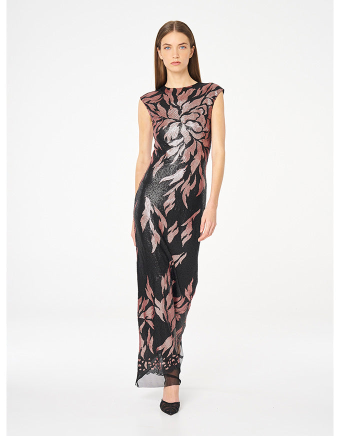 A woman modeling a sleeveless black maxi dress with a pink and gray floral pattern, photographed against a plain white studio background.