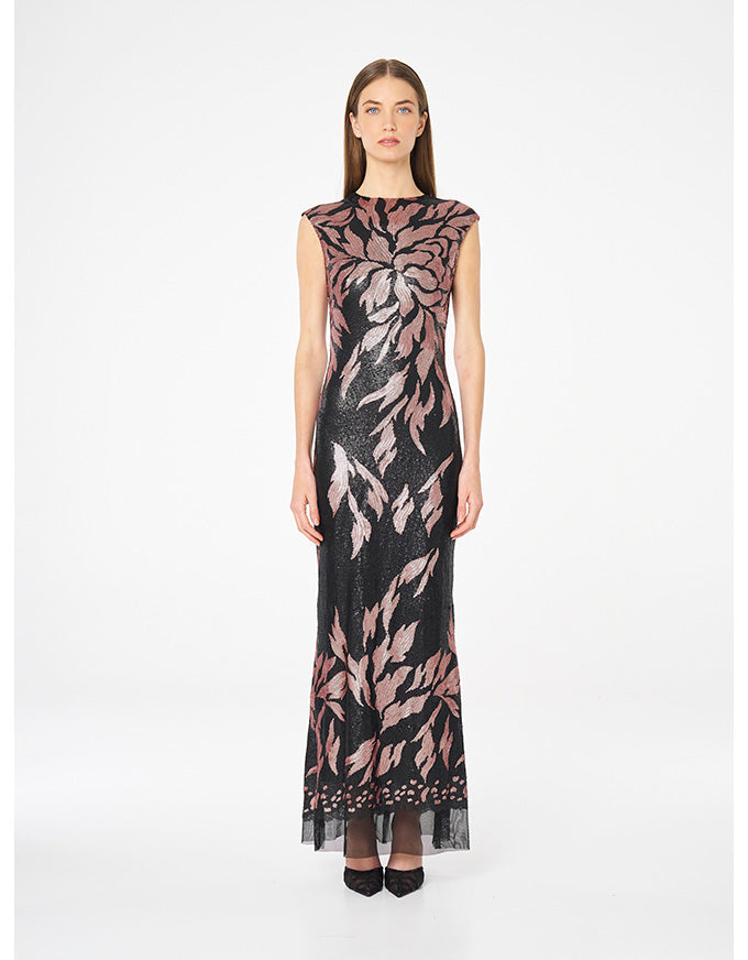 A woman modeling a sleeveless black maxi dress with a pink and gray floral pattern, photographed against a plain white studio background.