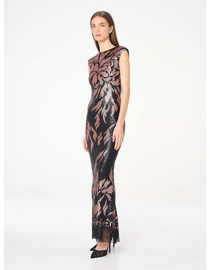 A model wearing a sleeveless, floor-length black dress with a metallic rose gold floral pattern, standing against a plain white studio background.
