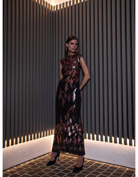 A woman models a sleeveless black midi dress with a metallic rose gold leaf pattern, standing in a modern room with vertical slatted walls.