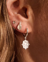 Close-up of an ear with multiple earrings on a warm-toned background