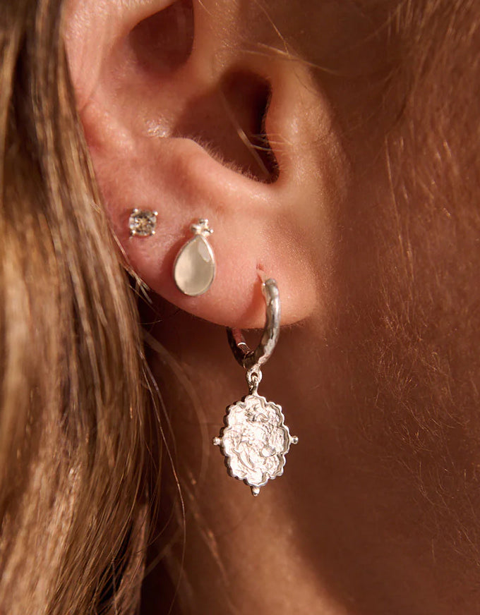 Close-up of an ear with multiple earrings on a warm-toned background
