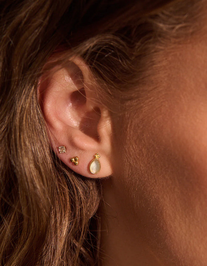 Close-up of an ear wearing gold earrings with a soft focus on hair and skin.