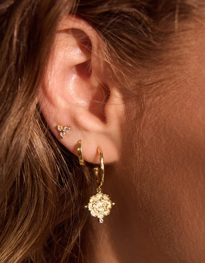 Close-up of an ear wearing gold hoop earrings with floral designs.