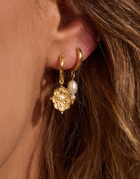 Close-up of a gold hoop earring with a pearl pendant worn by a person with brown hair.