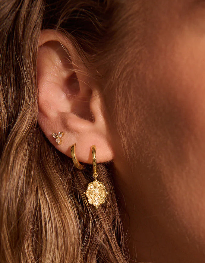 Close-up of an ear wearing gold earrings with a blurred background