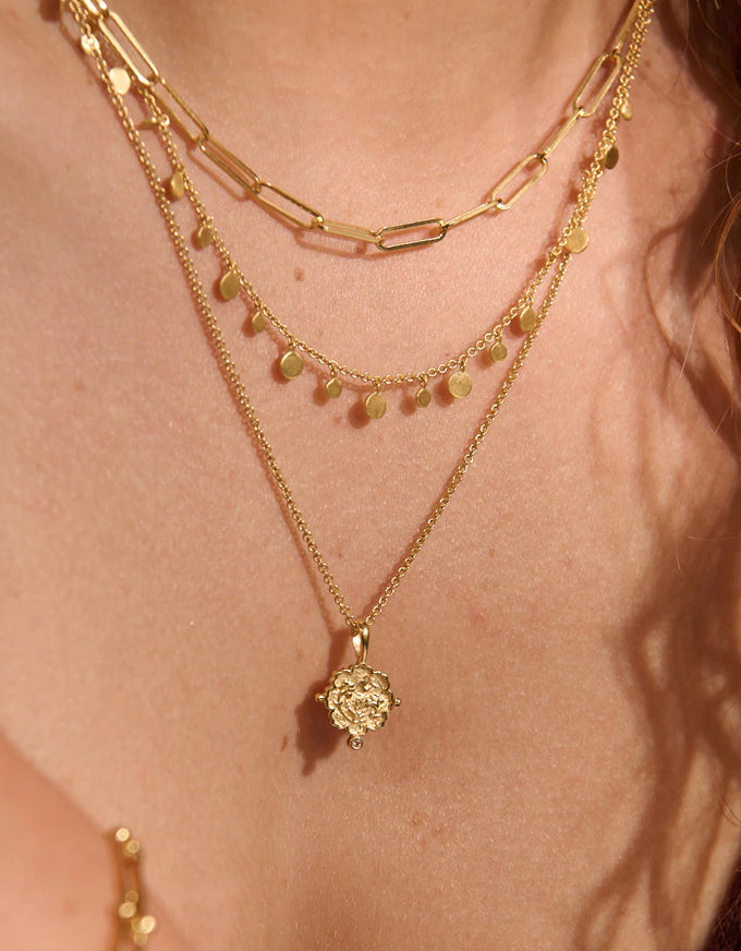 Close-up of a person wearing multiple gold necklaces with a focus on one necklace with a pendant.