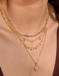 Close-up of a person wearing multiple gold necklaces with a pink beaded necklace.