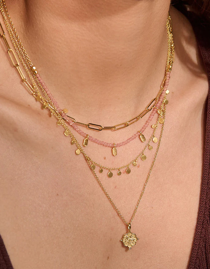 Close-up of a person wearing multiple gold necklaces with a pink beaded necklace.
