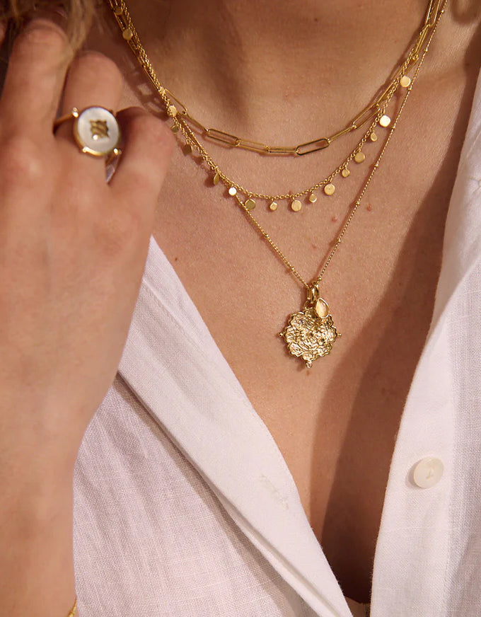 Close-up of a person wearing gold necklaces and a ring on a white shirt.