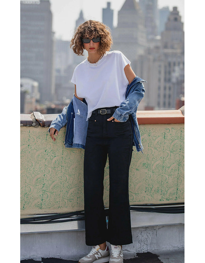 Person wearing a white t-shirt, black pants, and a denim jacket on a rooftop with city skyline in the background