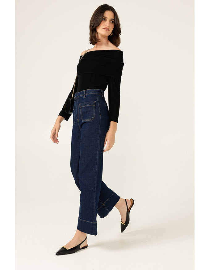 Woman wearing a black off-shoulder top and dark blue jeans on a white background