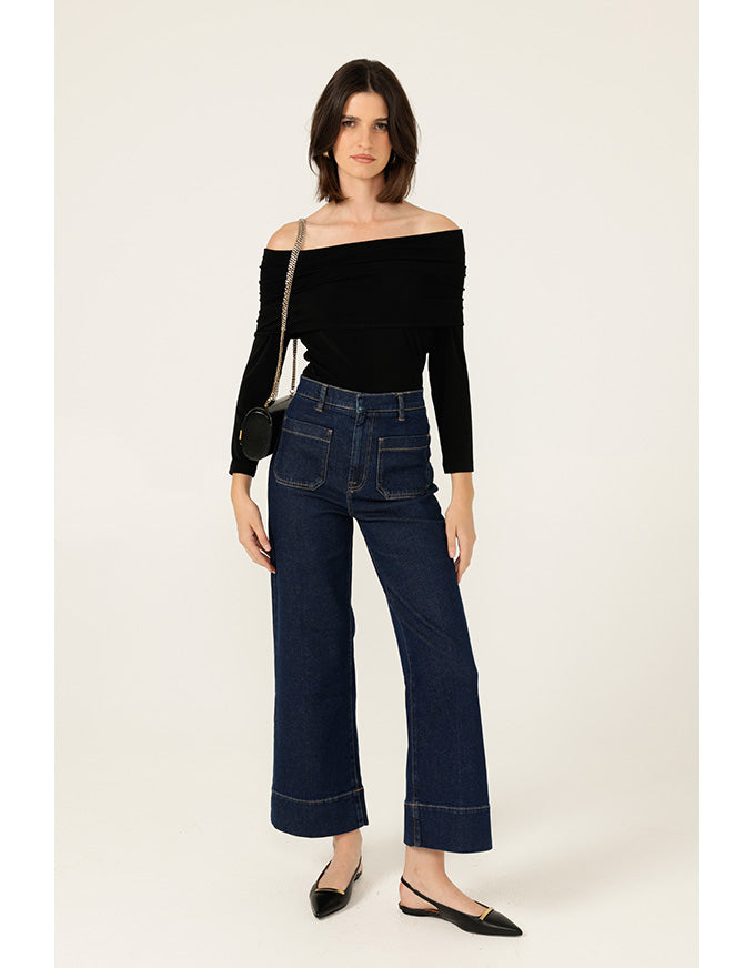 Woman wearing a black off-shoulder top and dark blue jeans on a white background