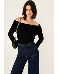 Woman wearing a black off-shoulder top and blue jeans with a white background