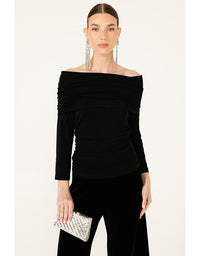 Woman wearing a black off-shoulder top with long sleeves, holding a clutch against a white background