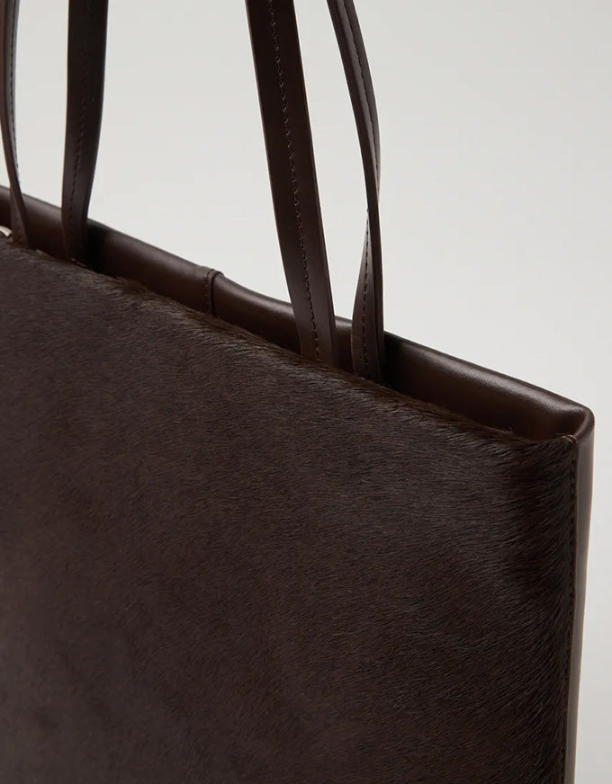 Close-up of a dark brown leather tote bag with visible texture.