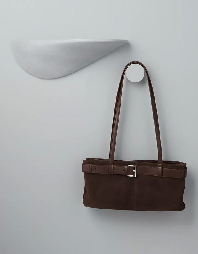 Brown handbag hanging on a white wall hook against a light gray background