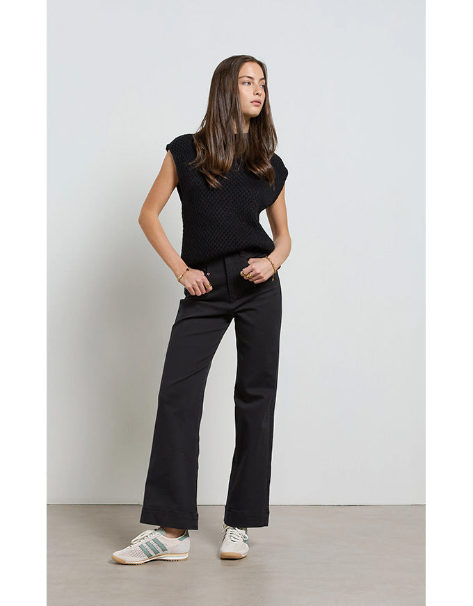 Woman wearing a black sleeveless top and black pants against a white background