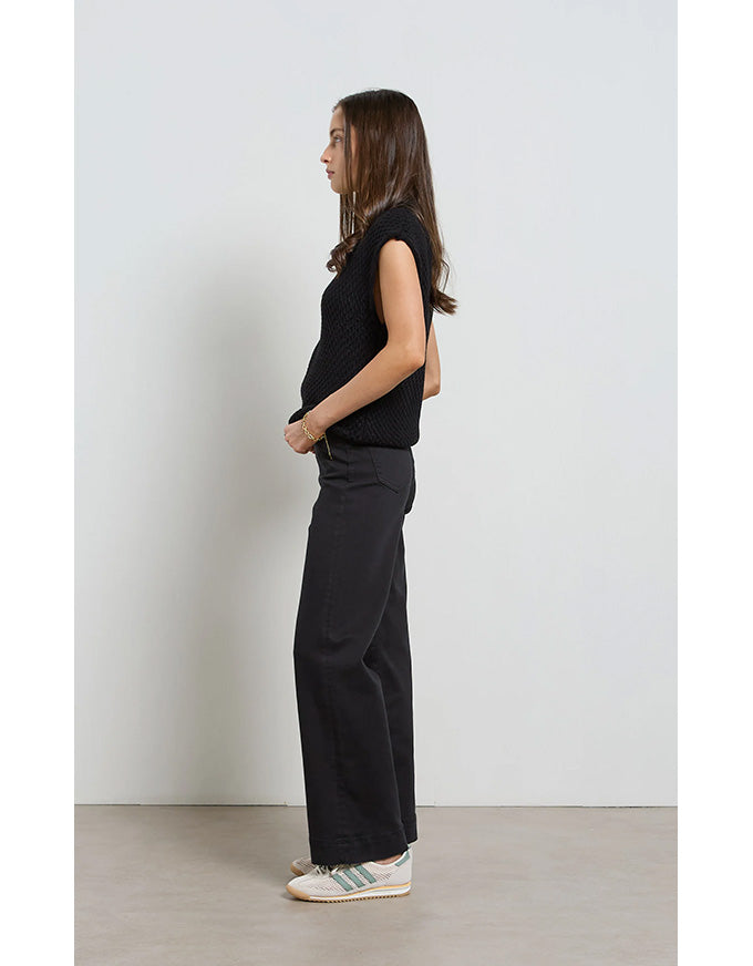 Person wearing a black outfit standing against a white wall