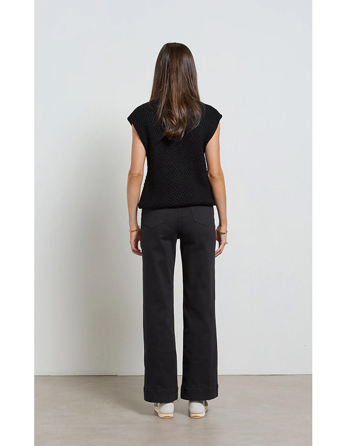 Woman wearing a black sleeveless top and black pants against a white background