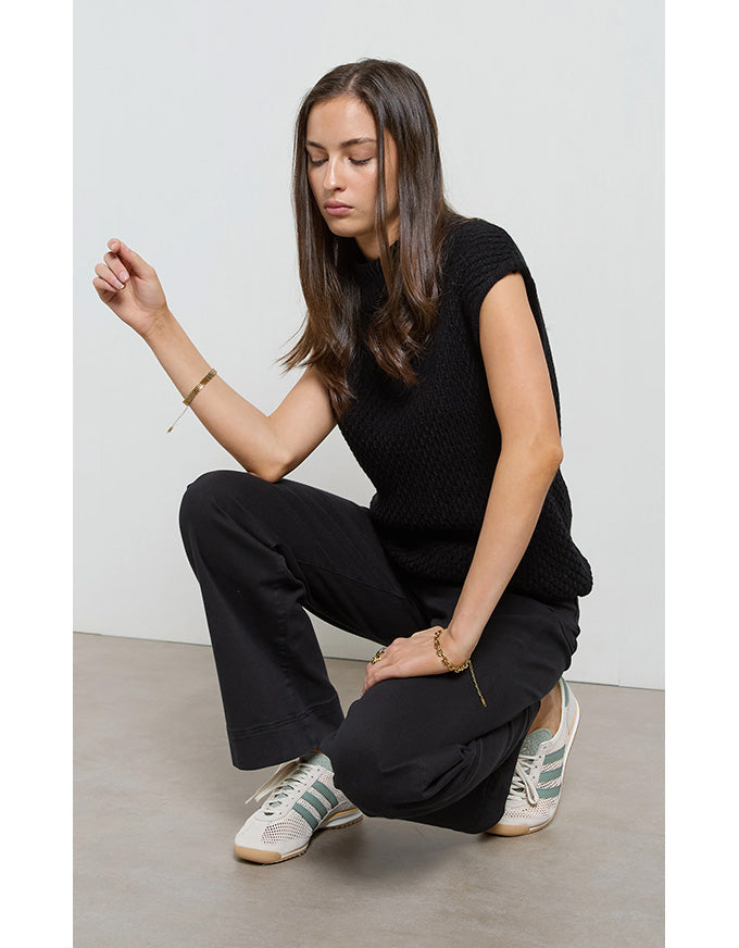 Woman in black outfit with white sneakers sitting on a light-colored floor against a plain white wall.