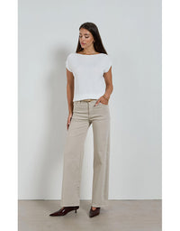 Woman wearing a white top and beige pants against a plain background