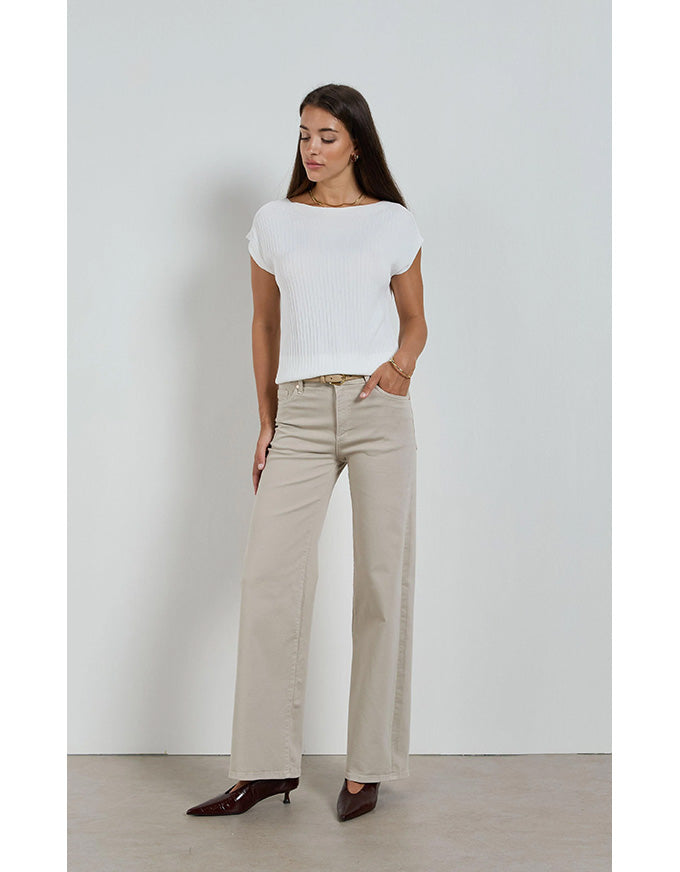 Woman wearing a white top and beige pants against a plain background