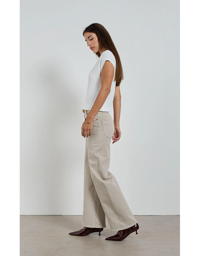 Woman wearing a white top and beige pants against a plain background