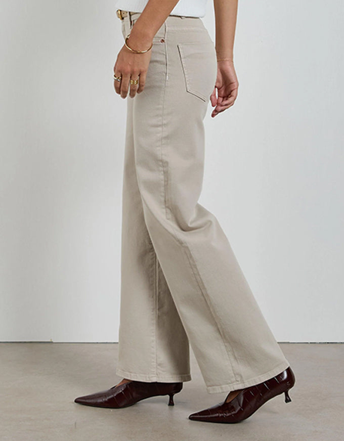 Person wearing beige wide-leg pants and brown shoes on a white background