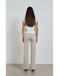 Woman wearing beige pants and a white top against a plain background