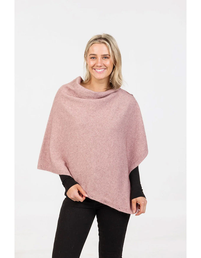 Woman wearing a pink poncho over a black top and pants on a white background