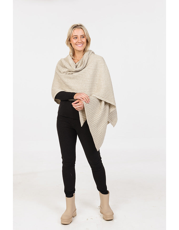 Woman wearing a beige poncho over a black outfit on a white background
