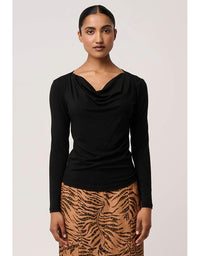 Woman wearing a black long-sleeve top and patterned skirt on a plain background
