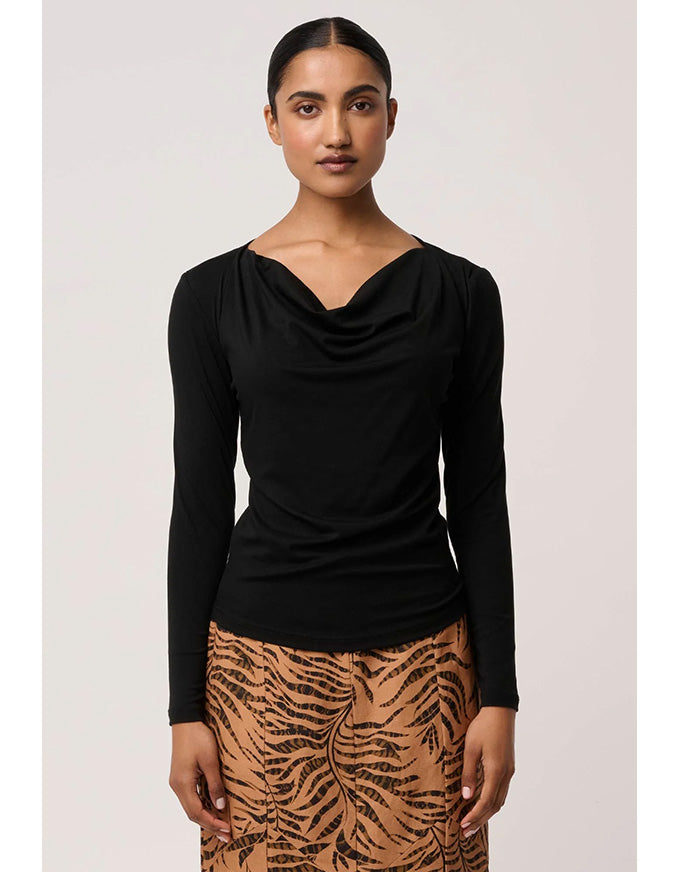 Woman wearing a black long-sleeve top and patterned skirt on a plain background