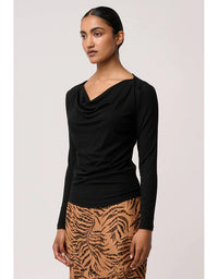 Woman wearing a black long-sleeve top and patterned skirt on a light pink background