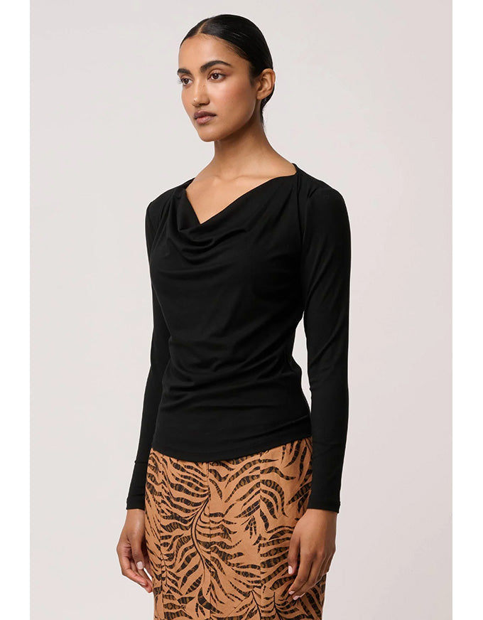 Woman wearing a black long-sleeve top and patterned skirt on a light pink background