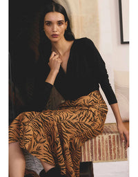 Woman wearing a black top and tiger print skirt sitting on a couch.