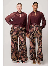 Two women wearing matching outfits with a burgundy top and patterned pants on a white background