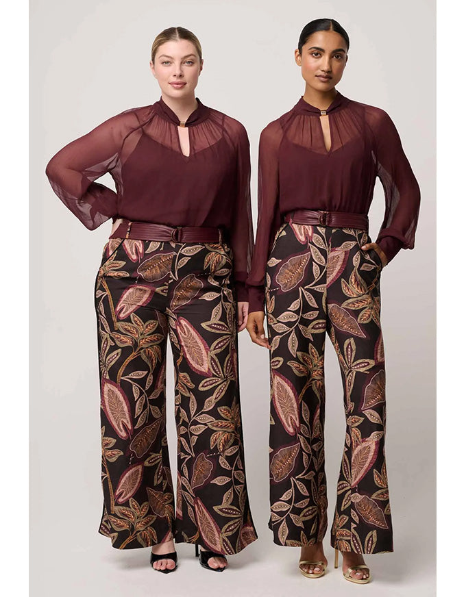 Two women wearing matching outfits with a burgundy top and patterned pants on a white background