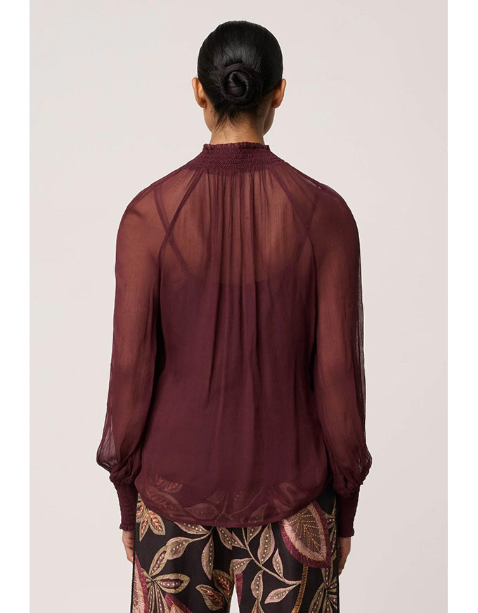 Person wearing a sheer burgundy blouse with patterned pants on a light pink background