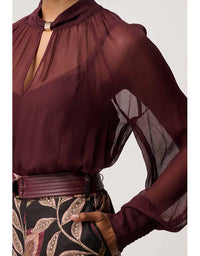Sheer burgundy blouse with long sleeves and a patterned belt on a white background