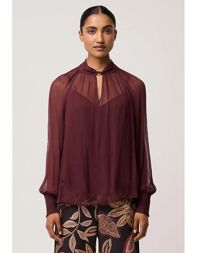 Woman wearing a burgundy blouse with sheer neckline against a white background